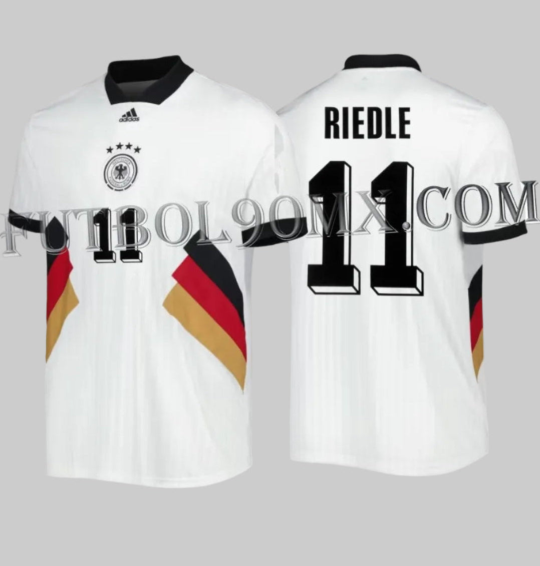 Vista dual del jersey adidas HS5941 Alemania Icon 2022. Frente con escudo DFB centrado y bloques tricolores; dorso con personalización oficial de leyenda RIEDLE y número 11 en tipografía 3D.