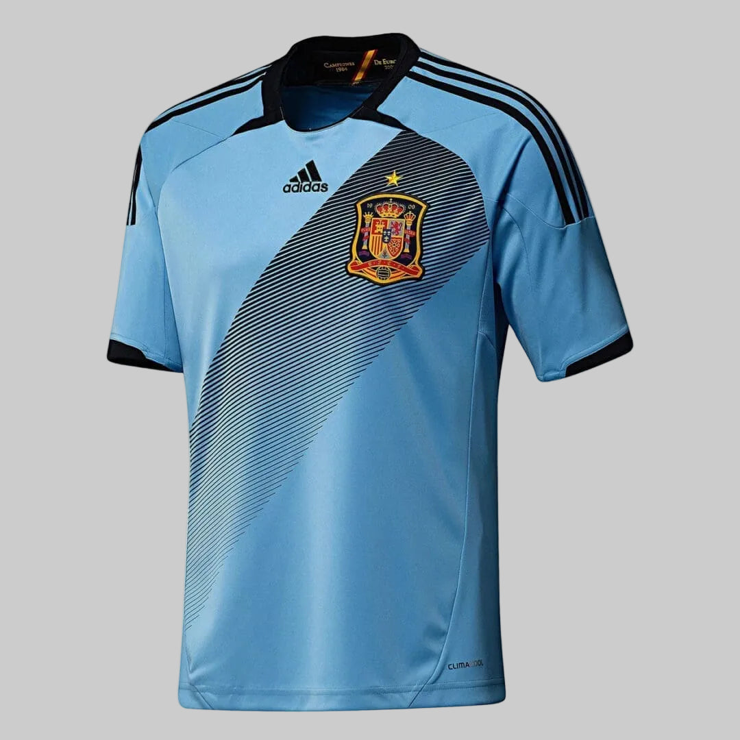 Vista frontal del jersey Adidas de España visita 2012/13 en azul celeste, destacando el dorsal frontal #6 de Andrés Iniesta y el diseño de banda diagonal texturizada.