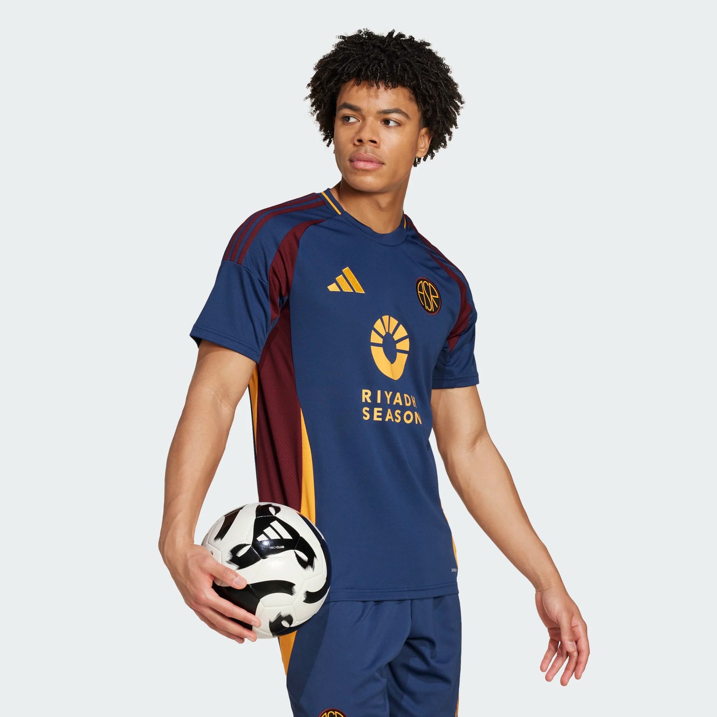 Vista lateral del jersey de la Roma 2024/25 mostrando las franjas asimétricas que combinan el rojo granate y el amarillo. Se aprecia la textura del panel lateral diseñada para ventilación técnica."