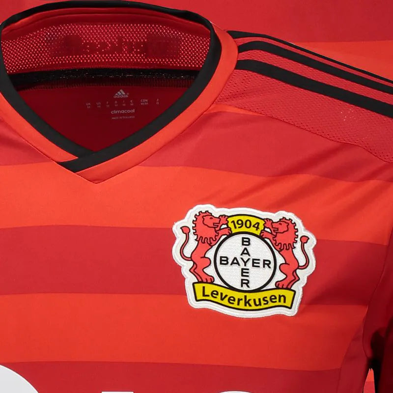Primer plano del cuello con la inscripción institucional "werkself", el escudo bordado del Bayer Leverkusen y los detalles en negro sobre la base roja (Código: F51271) en Futbol90MX.