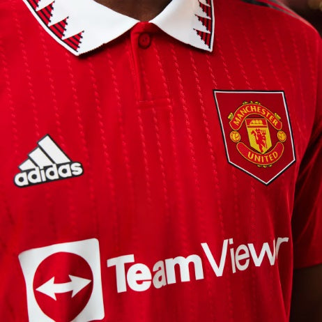 Acercamiento al cuello tipo polo del jersey Manchester United 2022/23 con diseño geométrico inspirado en los años 90 y botones ocultos.