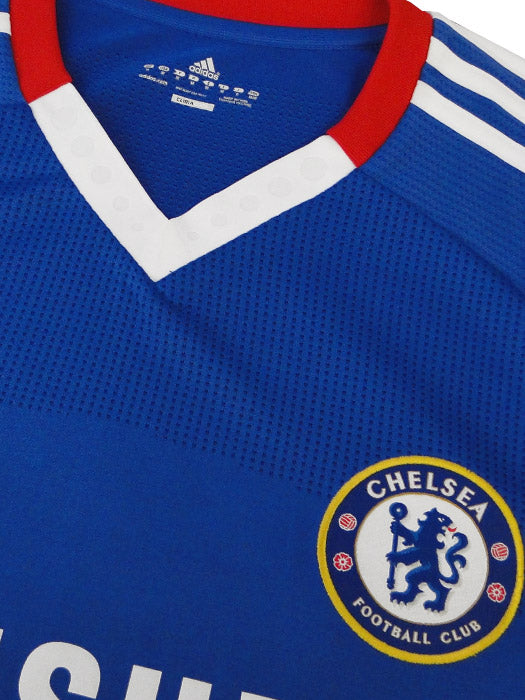 Primer plano del escudo bordado y del cuello del jersey Chelsea FC 2010/11, destacando los detalles en rojo y blanco con la etiqueta técnica de autenticidad