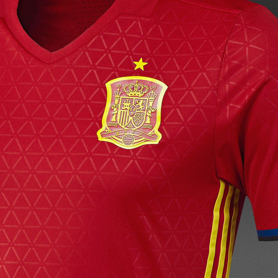 Acercamiento al escudo termotransferido y al patrón de triángulos en relieve sobre el tejido rojo, simbolizando la estructura táctica y el juego de posición de la selección en 2016.