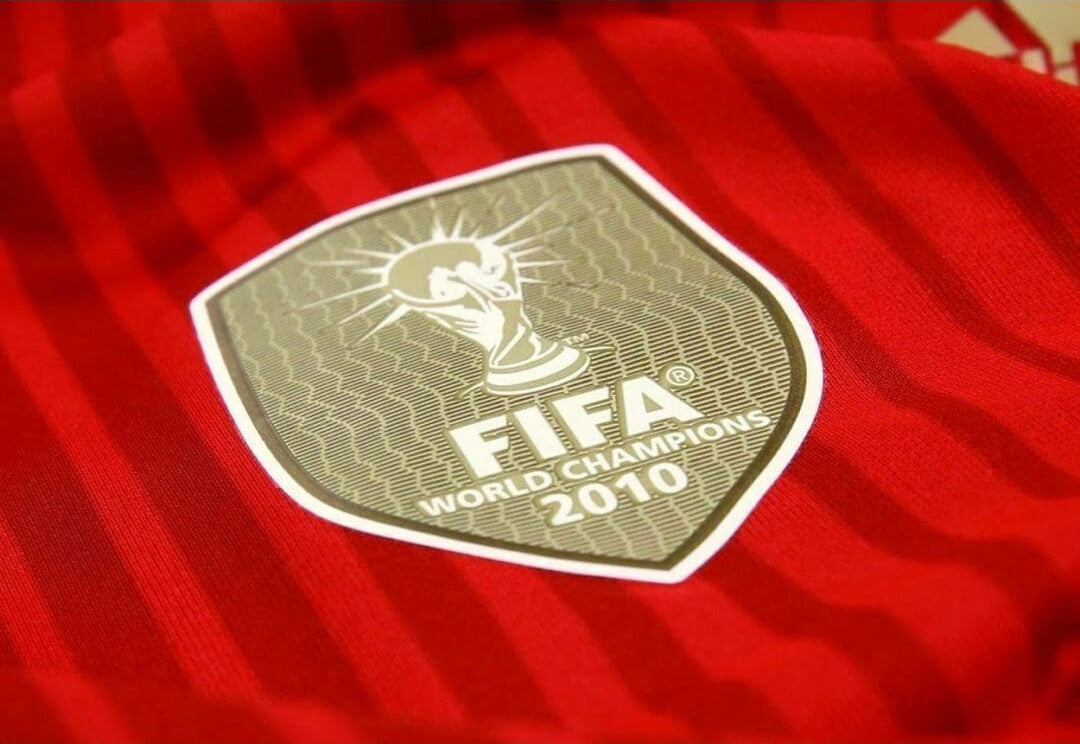 Acercamiento al parche oficial de 'FIFA World Cup Champions 2010' aplicado por transferencia térmica sobre el costado derecho del jersey.