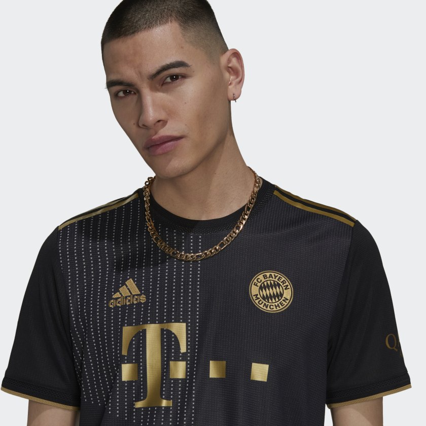 Primer plano de modelo luciendo el Adidas Musiala FC Bayern Munich Authentic Match Away Jersey UCL 2021/22 con el escudo dorado, logotipo Adidas y patrocinador T-Mobile (Código: GM5312) en Futbol90MX.