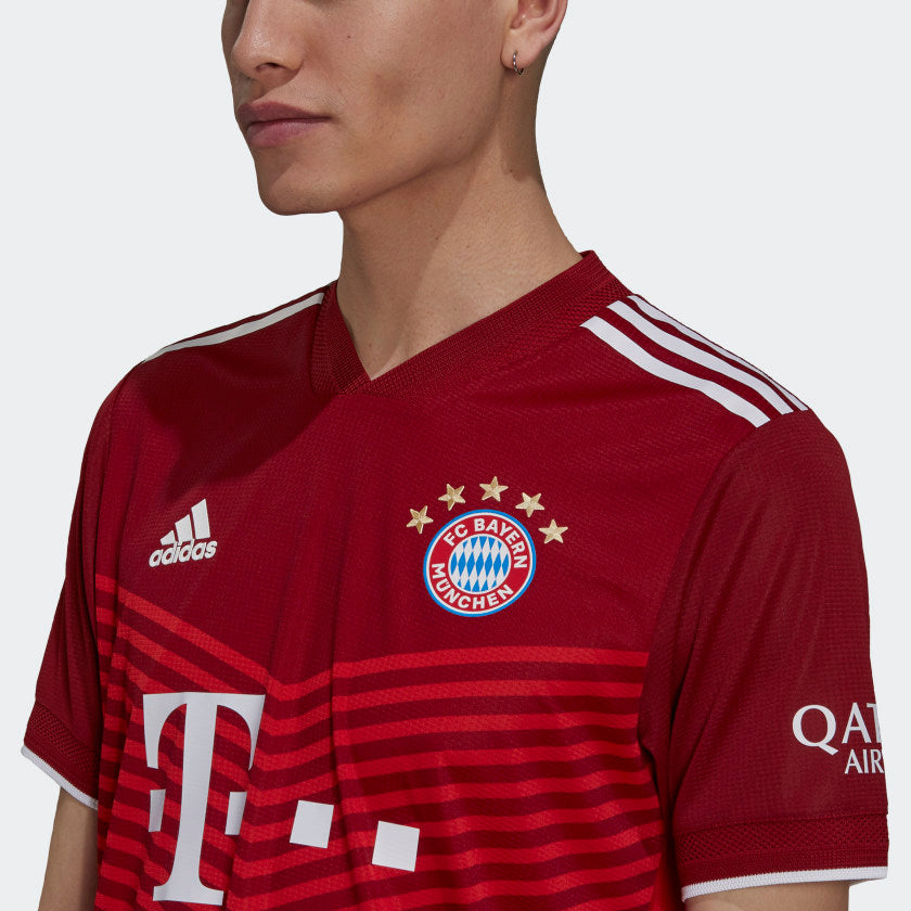 Primer plano de tres cuartos del jersey Adidas Authentic Match local del Bayern Múnich UCL 2021/22 de Kimmich (Ref. GM5308) sobre un modelo masculino, destacando el escudo con la quinta estrella dorada, el patrocinador central 'T...' y el detalle del logo de 'QATAR AIRWAYS' en la manga con certificación de Futbol90MX.