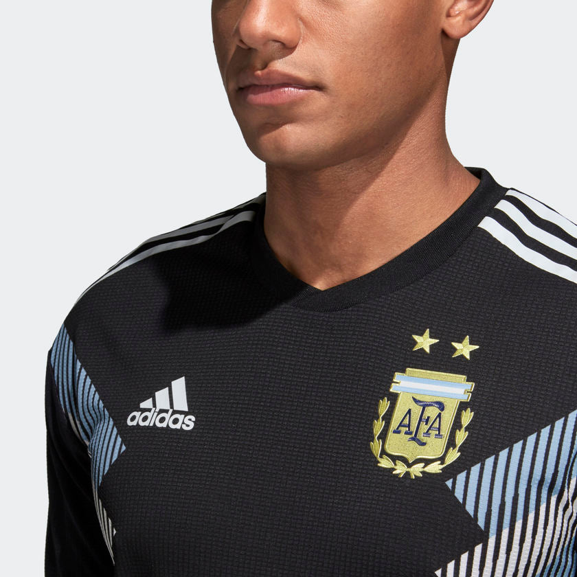 Primer plano del escudo de la Asociación del Fútbol Argentino (AFA) ap;icado en alta densidad con las dos estrellas sobre la textura técnica negra del jersey.