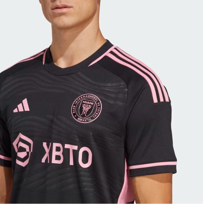 Primer plano de alta definición del pecho del jersey Authentic Match de Visita de Messi del Inter Miami (Ref. IC9621), resaltando el escudo termosellado del club y el logotipo 3-Bar de Adidas en color rosa, stock Futbol90MX