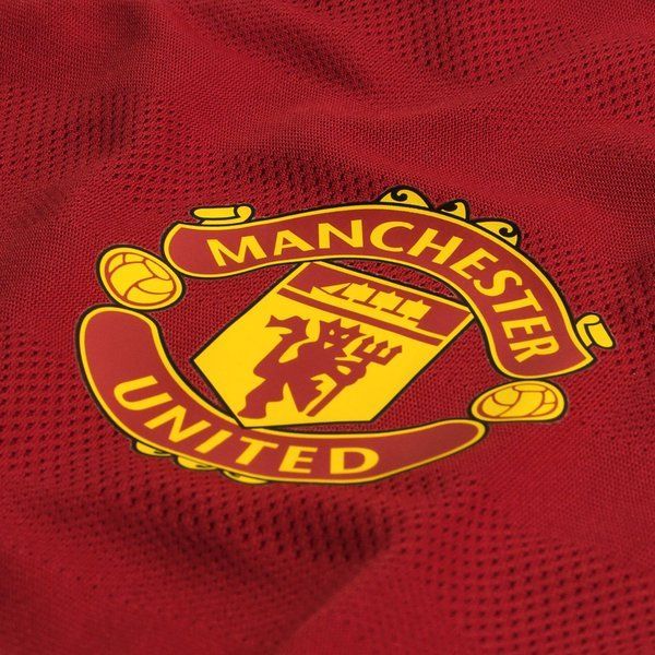 Primer plano macro del escudo oficial del Manchester United bordado en tonos rojo, amarillo y negro sobre la textura de malla técnica del jersey de local Adizero 2015/16 (Ref. AC1415).