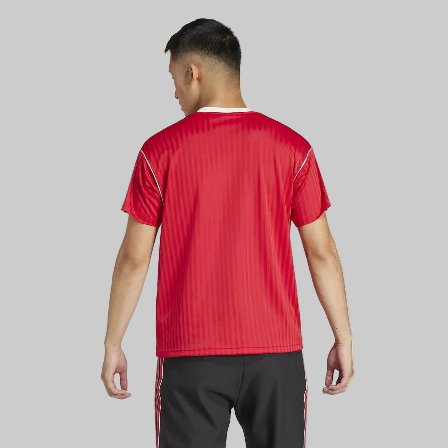Vista posterior de modelo portando el jersey Adidas Manchester United Icon (Ref. JF0386) mostrando la caída limpia del tejido rojo y los detalles blancos del cuello en Futbol90MX.