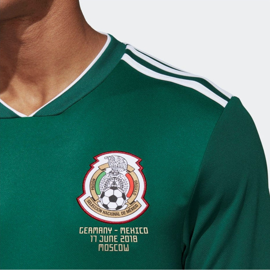 Acercamiento al escudo de la Selección Mexicana con la leyenda de partido "GERMANY VS. MEXICO – 17 JUNE 2018 – MOSCOW" termo-sellada con precisión bajo el emblema en Jersey Adidas Mexico manga larga mundial 2018 de Raul Jimenez