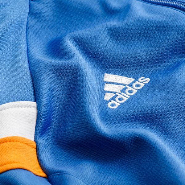 Detalle del logotipo de Adidas bordado en blanco sobre el tejido azul de la chamarra de pista Real Madrid Anthem 2013/14 (G89944), stock Futbol90MX