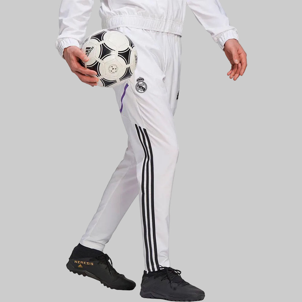 Vista lateral de perfil del modelo portando los pantalones Adidas Real Madrid 2022/23 (Ref. HA2592) y un balón clásico en la Historical Archive Boutique de Futbol90MX.