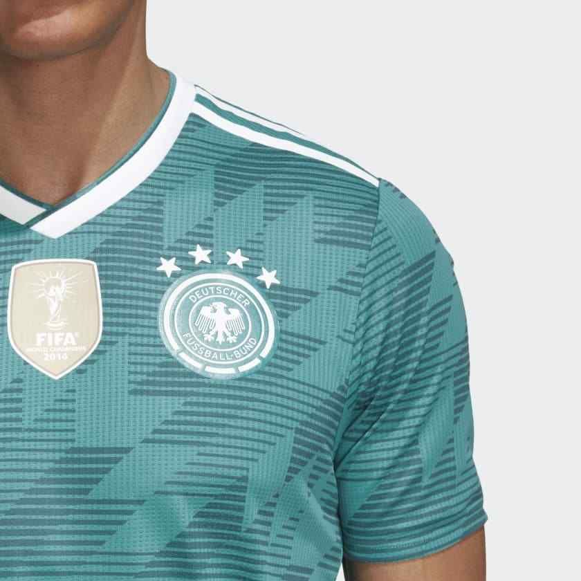Primer plano del escudo de la Federación Alemana (DFB) de alta densidad con las cuatro estrellas de campeón mundial sobre el tejido verde técnico del jersey authentic match de visita mundial 2018