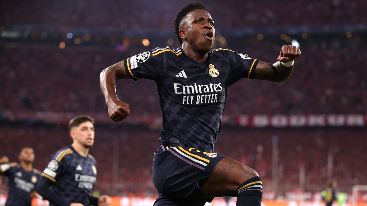Fotografía de acción de Vinícius Júnior celebrando gol con la indumentaria visitante del Real Madrid con parches oficiales de la UEFA Champions League 2023/24 en Futbol90MX.