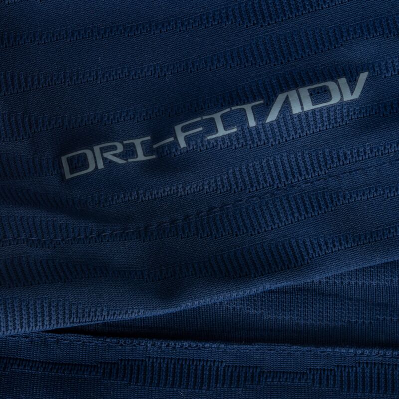 Primer plano de la tecnología de rendimiento aplicada. Muestra el logotipo "DRI-FIT ADV" termosellado en gris plateado sobre la textura técnica estriada del tejido elástico del jersey Jordan Mbappe PSG Local UCL 2021/22.