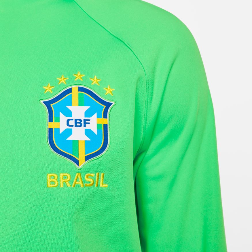 Acercamiento al escudo bordado de la CBF con las cinco estrellas doradas sobre el tejido de punto premium de la chamarra Anthem Brasil 2022.