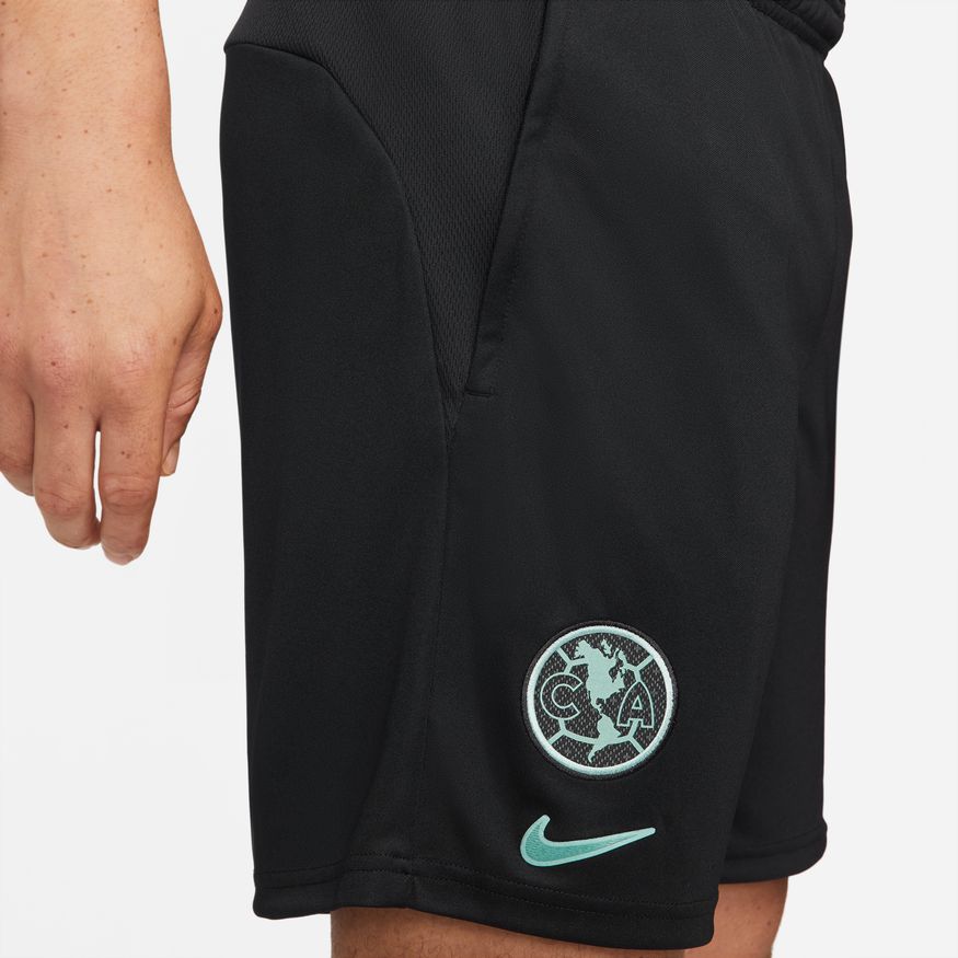 Acercamiento al escudo del Club América y Swoosh de Nike en color Verde Jade sobre tejido técnico negro de alta transpirabilidad.