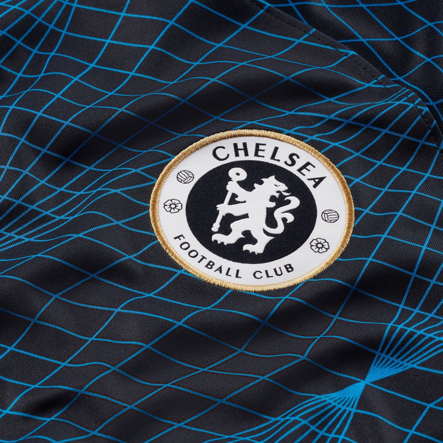 Detalle macro del escudo del Chelsea FC con acabado iridiscente sobre el tejido técnico Nike Dri-FIT.