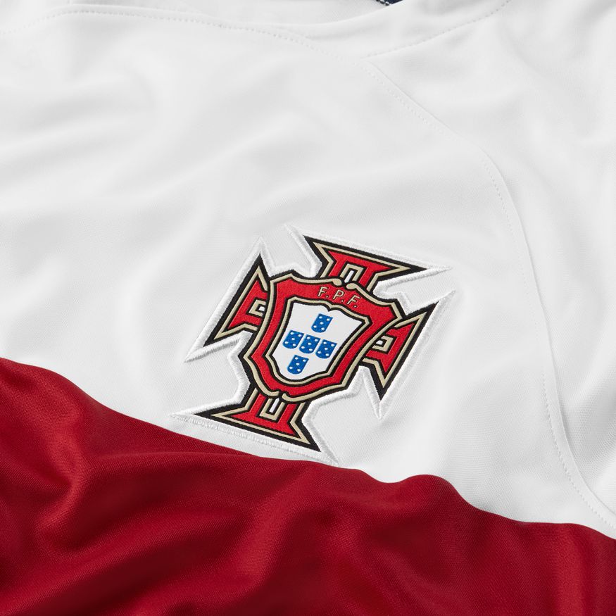 Primer plano del escudo de la Federação Portuguesa de Futebol bordado en alta densidad sobre la textura blanca del jersey de visita Nike 2022 de Cristiano Ronaldo.