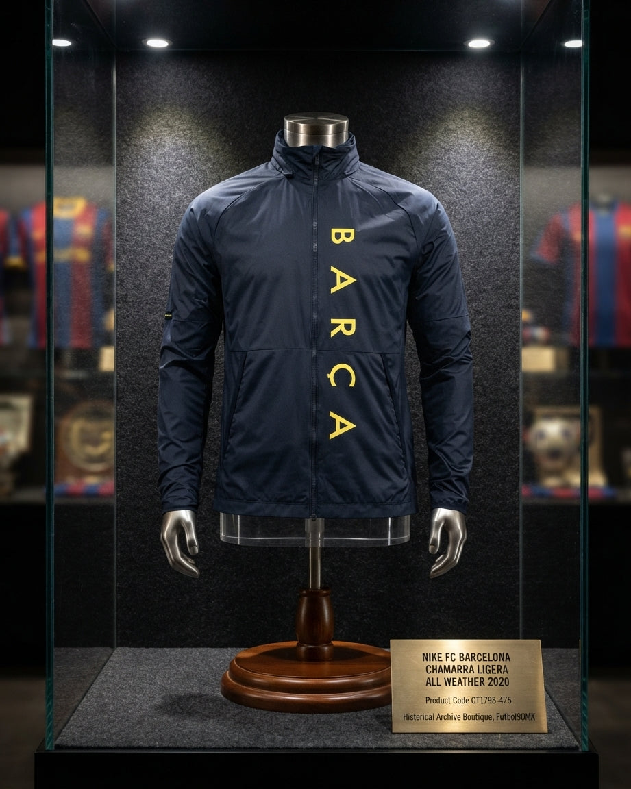 Exhibición museográfica de la chamarra ligera Nike FC Barcelona All Weather 2020 (Ref. CT1793-475) en una vitrina de cristal iluminada, con base metálica, placa conmemorativa y el uniforme completo de archivo en la Historical Archive Boutique de Futbol90MX. 🏛️⚽✨