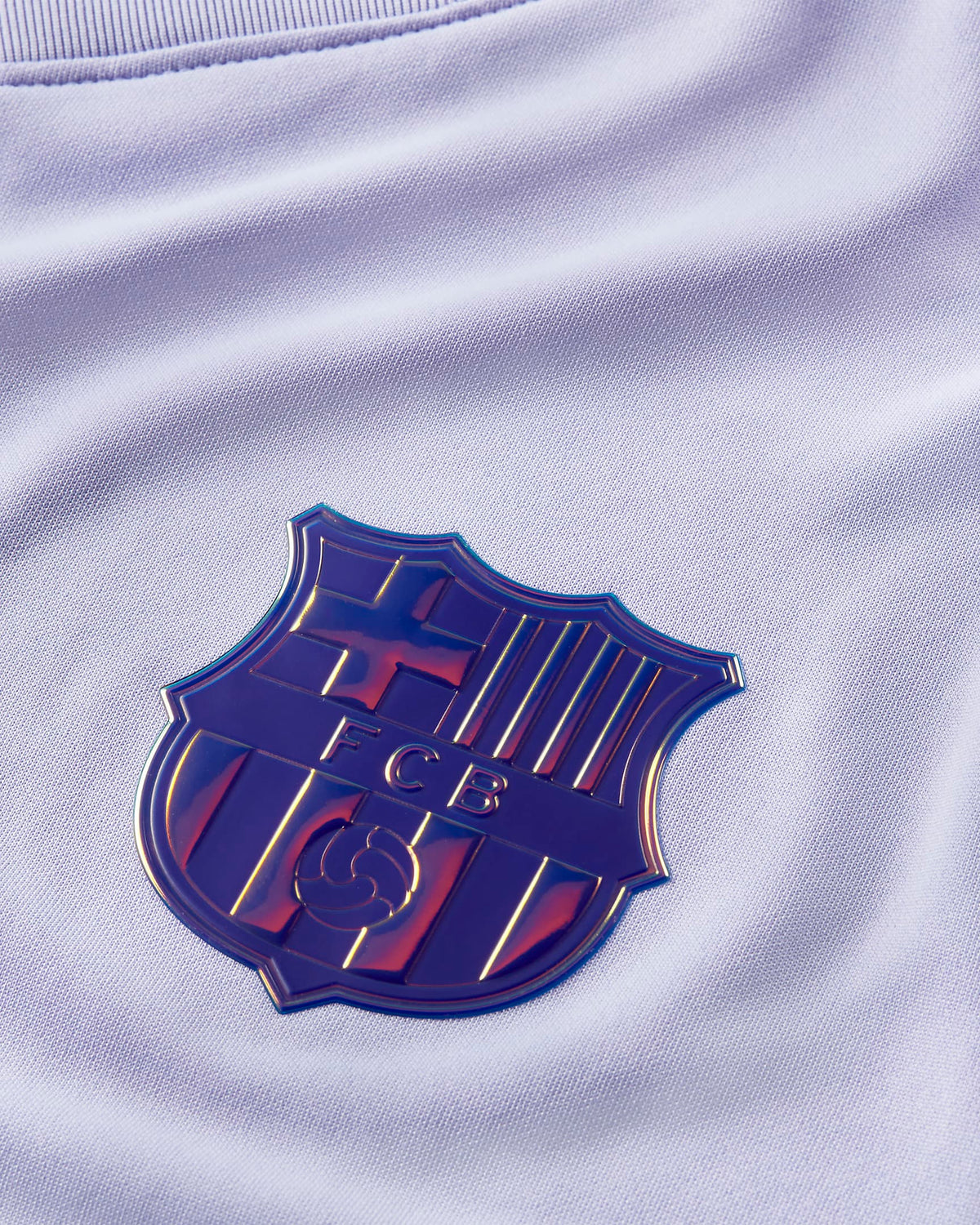 Primer plano del escudo del FC Barcelona con acabado iridiscente y tornasol sobre el tejido violeta claro del jersey de visita 2021/22 (CV7890-581) en Futbol90MX