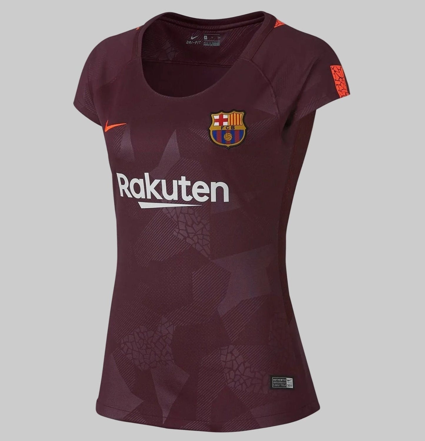 Vista angulada de la tercera equipación femenina del FC Barcelona, temporada 2017/18, en color granate sobre fondo de concreto, mostrando el logo de 'Rakuten', el escudo y el swoosh de Nike en naranja neón, codigo 847224-683, disponible en Futbol90MX
