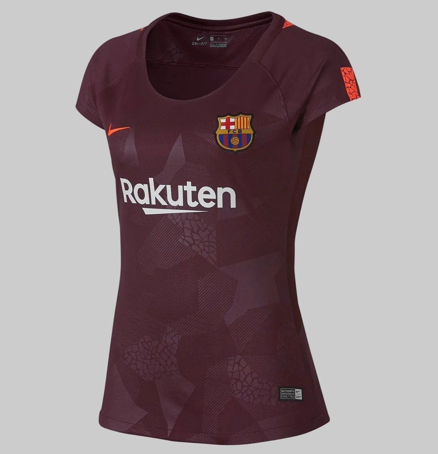 Vista angulada de la tercera equipación femenina del FC Barcelona, temporada 2017/18, en color granate sobre fondo de concreto, mostrando el logo de 'Rakuten', el escudo y el swoosh de Nike en naranja neón, codigo 847224-683, disponible en Futbol90MX