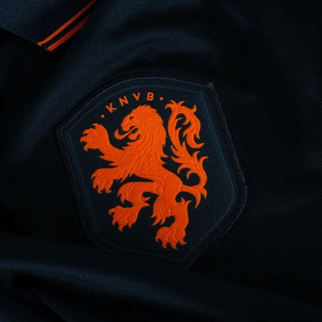 Primer plano del escudo de la KNVB bordado con precisión en naranja vibrante sobre el tejido negro de alta densidad