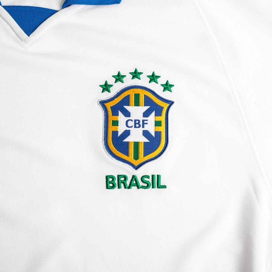 Primer plano del cuello tipo polo azul y el escudo de la CBF sobre el tejido blanco conmemorativo del centenario (1919-2019).