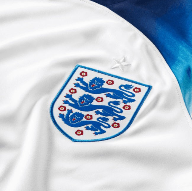 Primer plano del escudo oficial de la Selección de Inglaterra (The FA) bordado en el pecho del jersey de local 2022. Alta calidad y detalle de autenticidad.