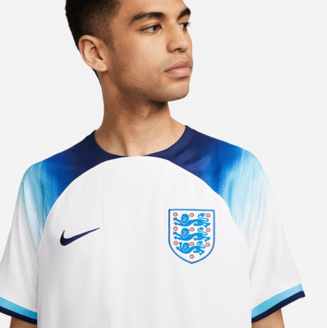 Primer plano del escudo de Inglaterra y el logotipo Nike Swoosh en azul marino, aplicado sobre el tejido técnico de alto rendimiento del jersey de Inglaterra, edición Copa Mundial 2022.