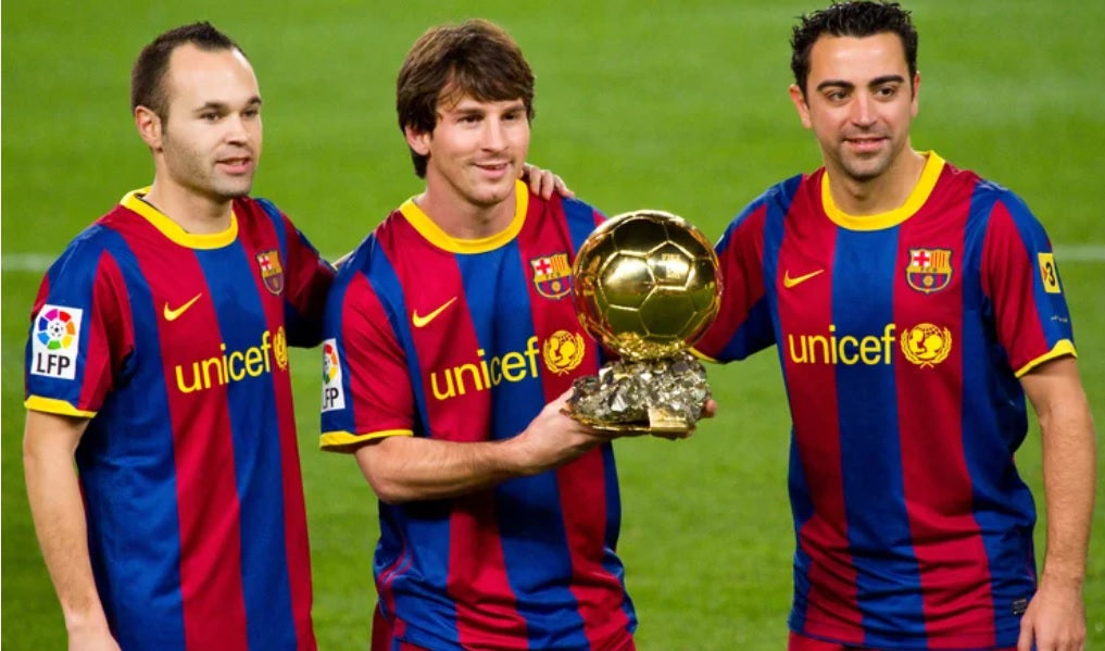Andrés Iniesta, Lionel Messi y Xavi Hernández sosteniendo el Balón de Oro con el uniforme local del FC Barcelona 2010/11 (Ref. 406809-486) en Futbol90MX