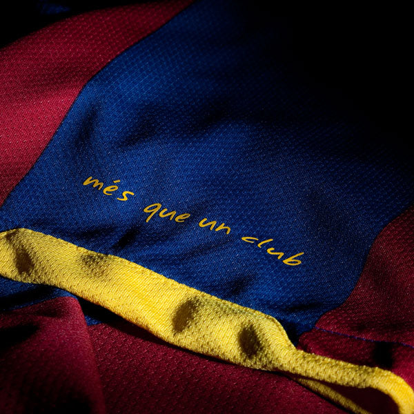 Primer plano de la frase "més que un club"  termo aplicada en la manga izquierda del jersey Authentic Match local FC Barcelona 2010/11 de Messi (Ref. 406809-486) en Futbol90MX.