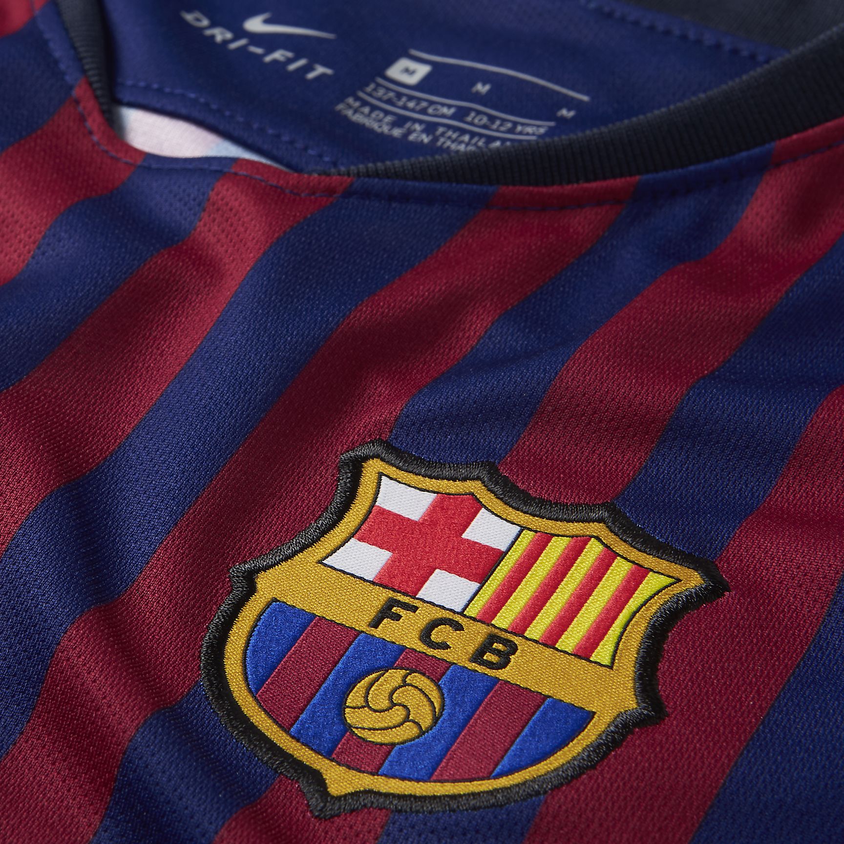 Acercamiento al escudo bordado del FC Barcelona y el logo de Nike sobre el diseño de 10 franjas simétricas que representan los distritos de la ciudad en la temporada 2018/19.