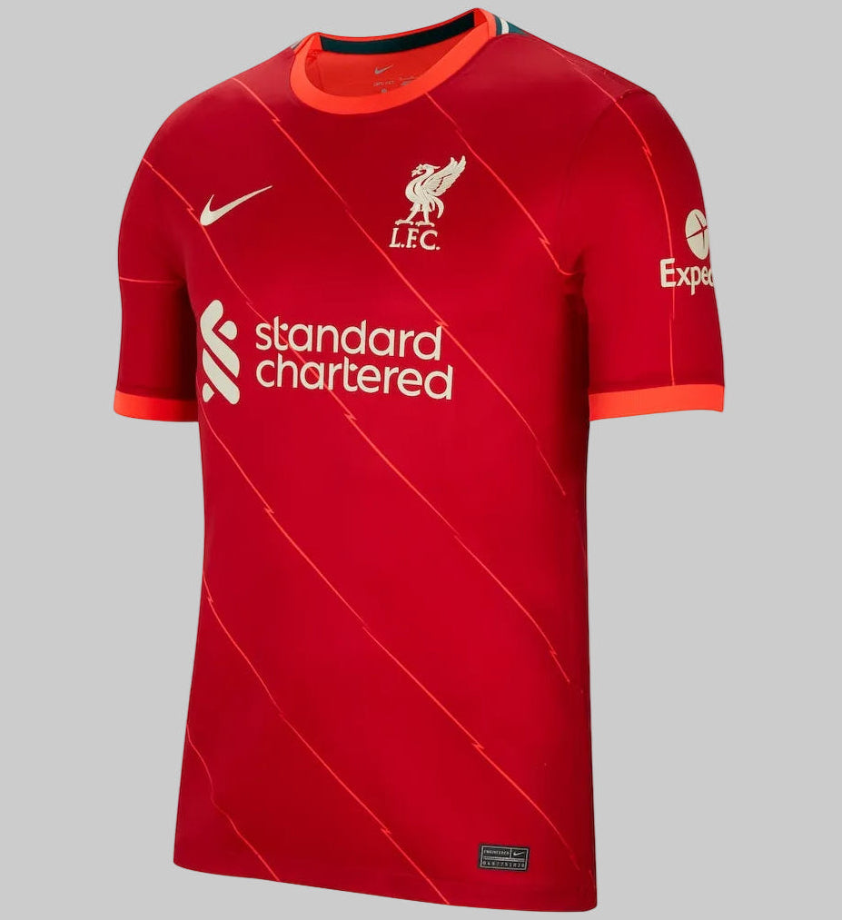 Vista frontal del jersey Nike Stadium local del Liverpool FC (DB2560-688) de la temporada 2021/22, mostrando el icónico color rojo intenso con líneas diagonales de rayos, el escudo del club y el patrocinador Standard Chartered en Futbol90MX