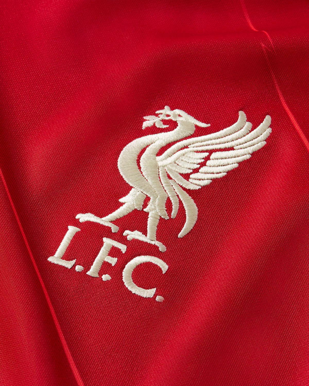 Primer plano de alta definición del escudo tradicional del Liverbird bordado en color blanco sobre el tejido rojo con patrón de rayos del jersey del Liverpool FC (DB2560-688) en la Historical Archive Boutique de Futbol90MX