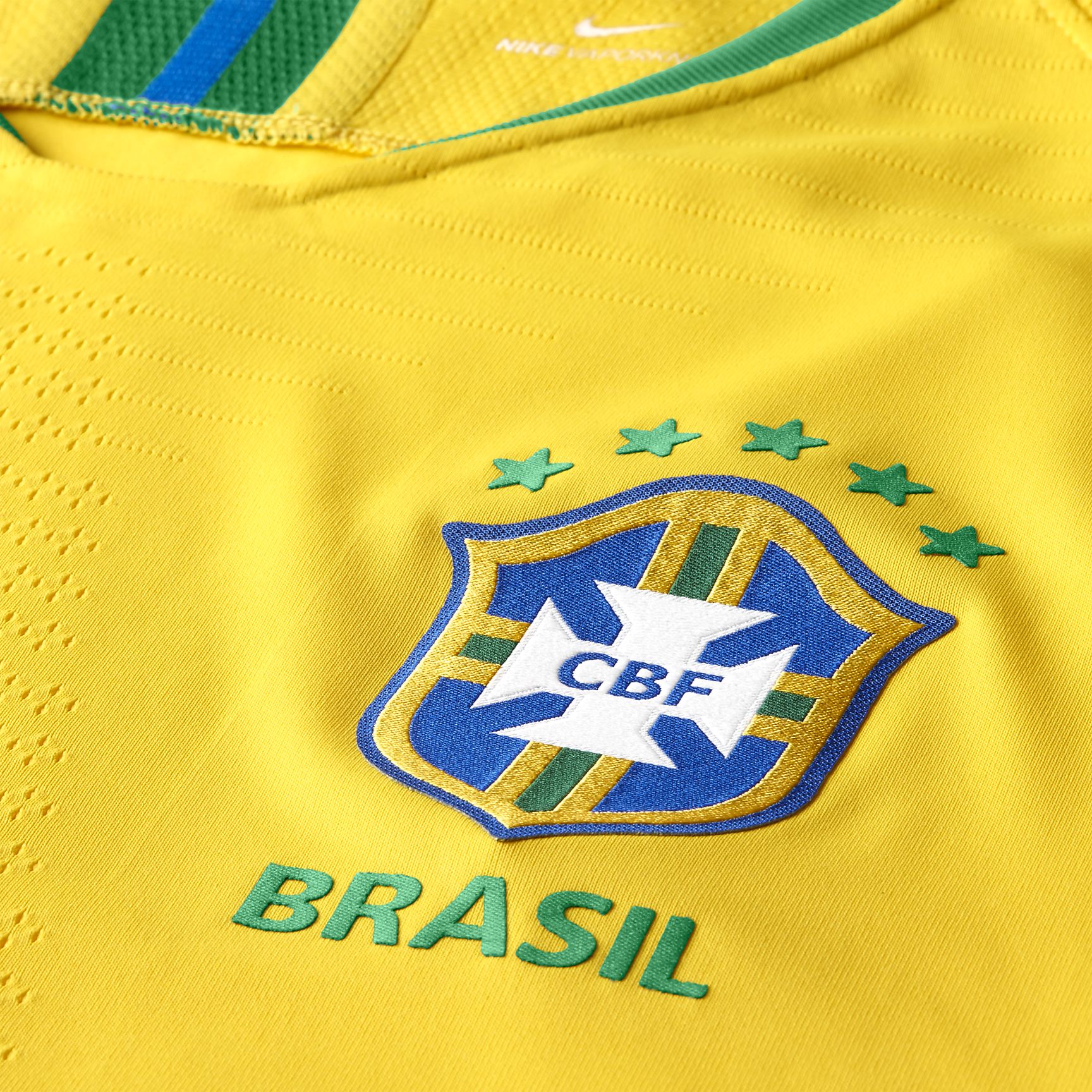 Detalle técnico del escudo de la CBF en alta densidad sobre tejido 'Samba Gold' y el patrón de tejido Vaporknit para ventilación dirigida, característico de la versión jugador.