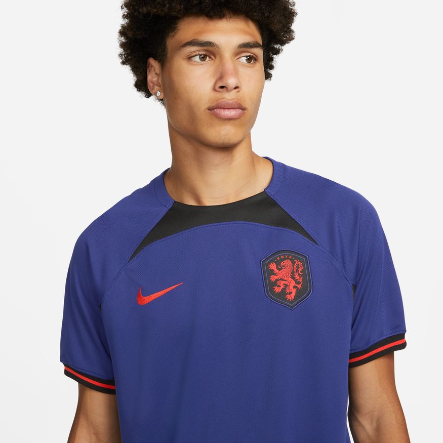 Primer plano del escudo de la Selección Neerlandesa y el logo de Nike en Habanero Red sobre el tejido técnico Dri-FIT del jersey 2022.