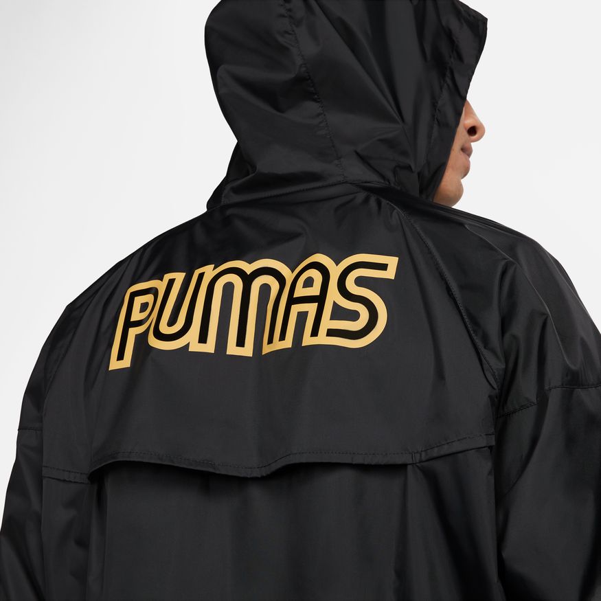 Primer plano del gráfico posterior de la chamarra Nike de Pumas UNAM 2023 con la palabra PUMAS estampada con contorno abierto dorado, codigo DX7963-014