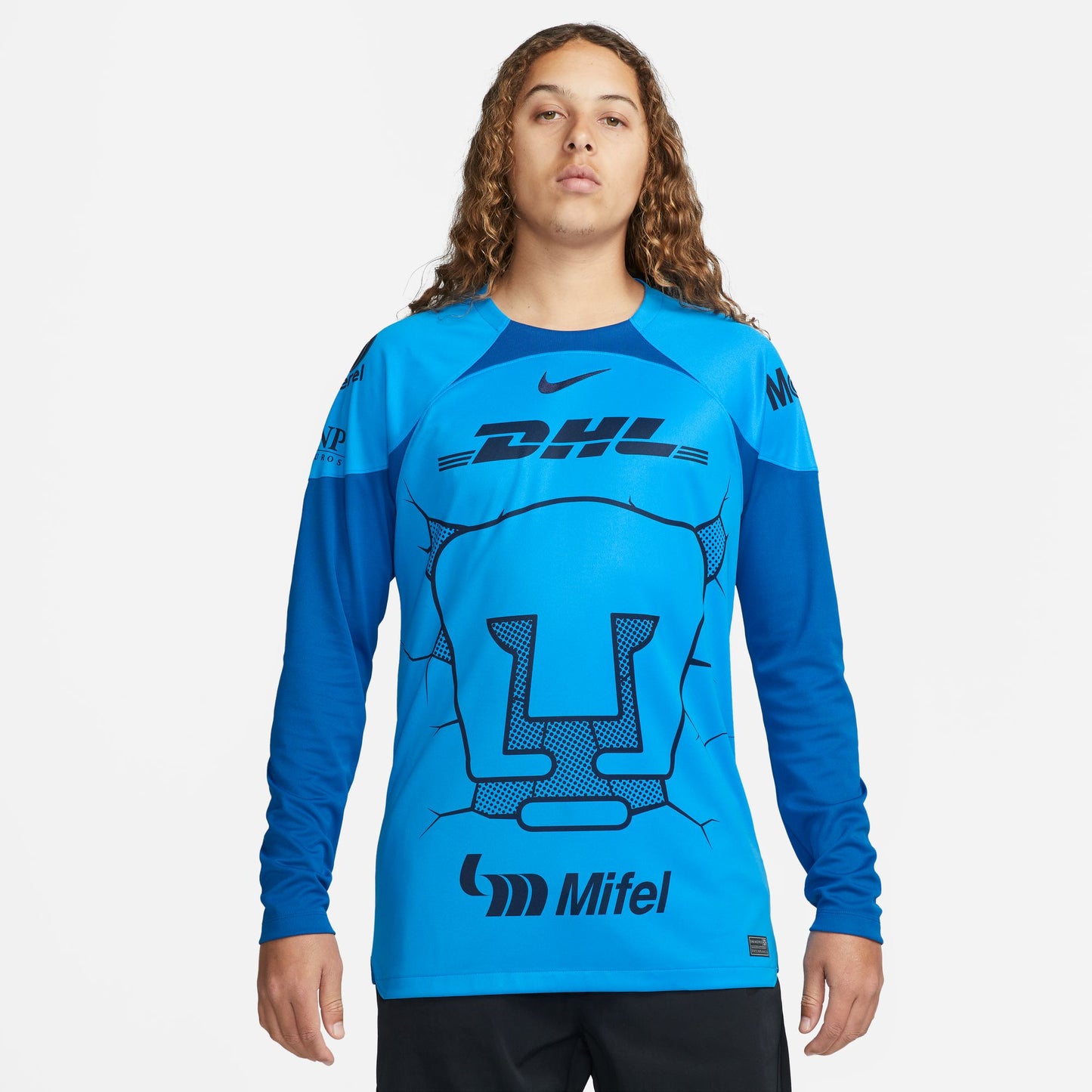 Primer plano del escudo sobredimensionado del Puma y patrón de grietas tonales en el pecho del jersey de portero Pumas 2023-24. Impresión de alta definición y logotipos de patrocinadores DHL y Mifel.