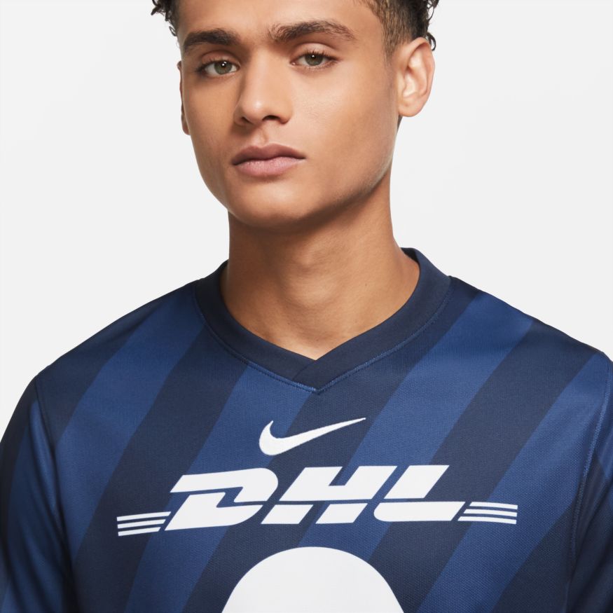 Detalle del escudo del Puma y patrocinador DHL en blanco monocromático sobre el tejido técnico azul marino.