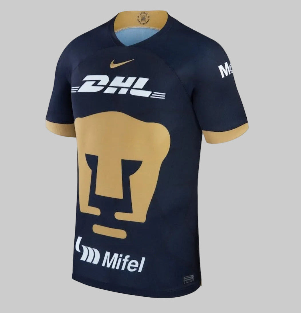 Perspectiva lateral del jersey Pumas 2023-24 mostrando los paneles de ventilación y el corte atlético Slim Fit. Detalles dorados en los puños de las mangas cortas Nike DX2638-407