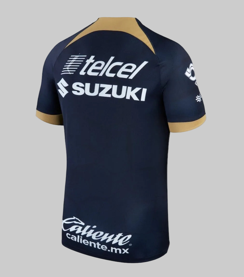 Vista posterior del jersey de visita Pumas UNAM 2023-24 en azul profundo con logotipos de Telcel y banca Mifel. Tejido microperforado para máxima transpirabilidad.