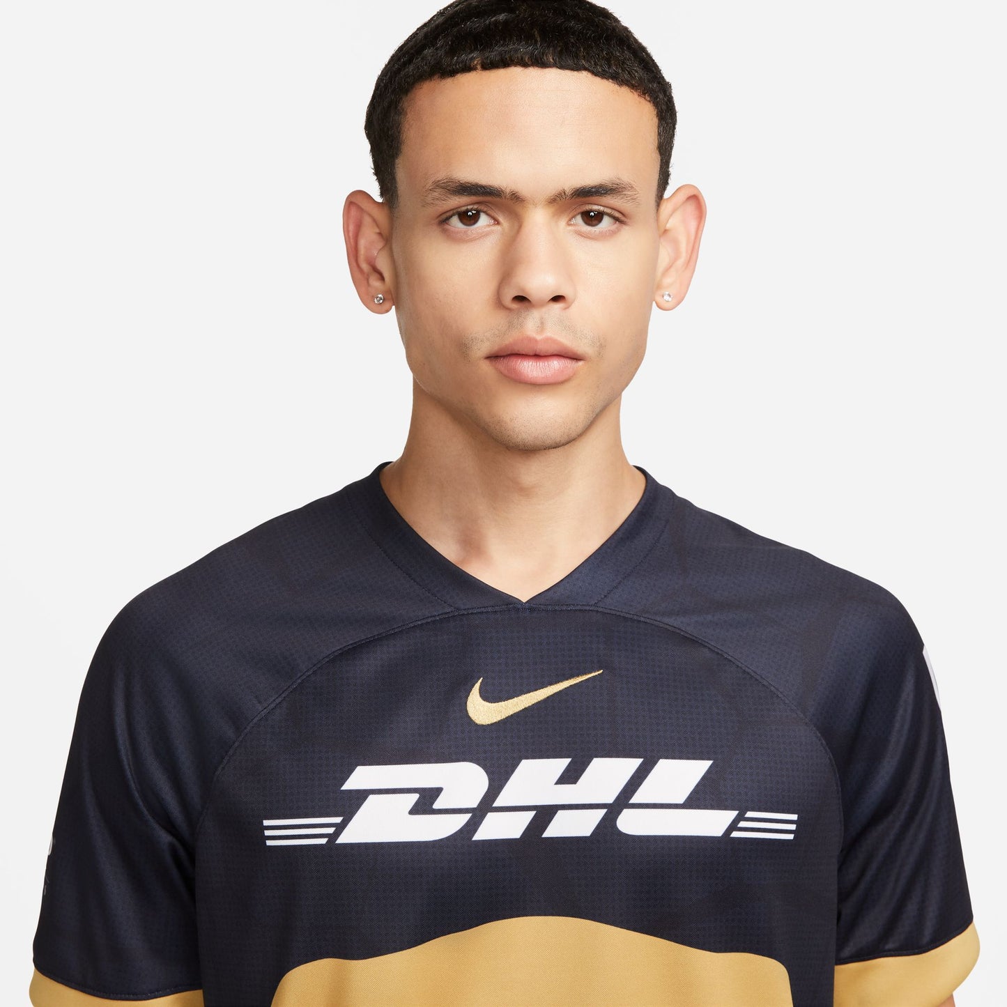 Primer plano del escudo del Puma en dorado universitario y el Nike Swoosh bordado en el jersey de visita 2023-24. Detalle del cuello redondo con ribete dorado y tecnología Nike Dri-FIT.