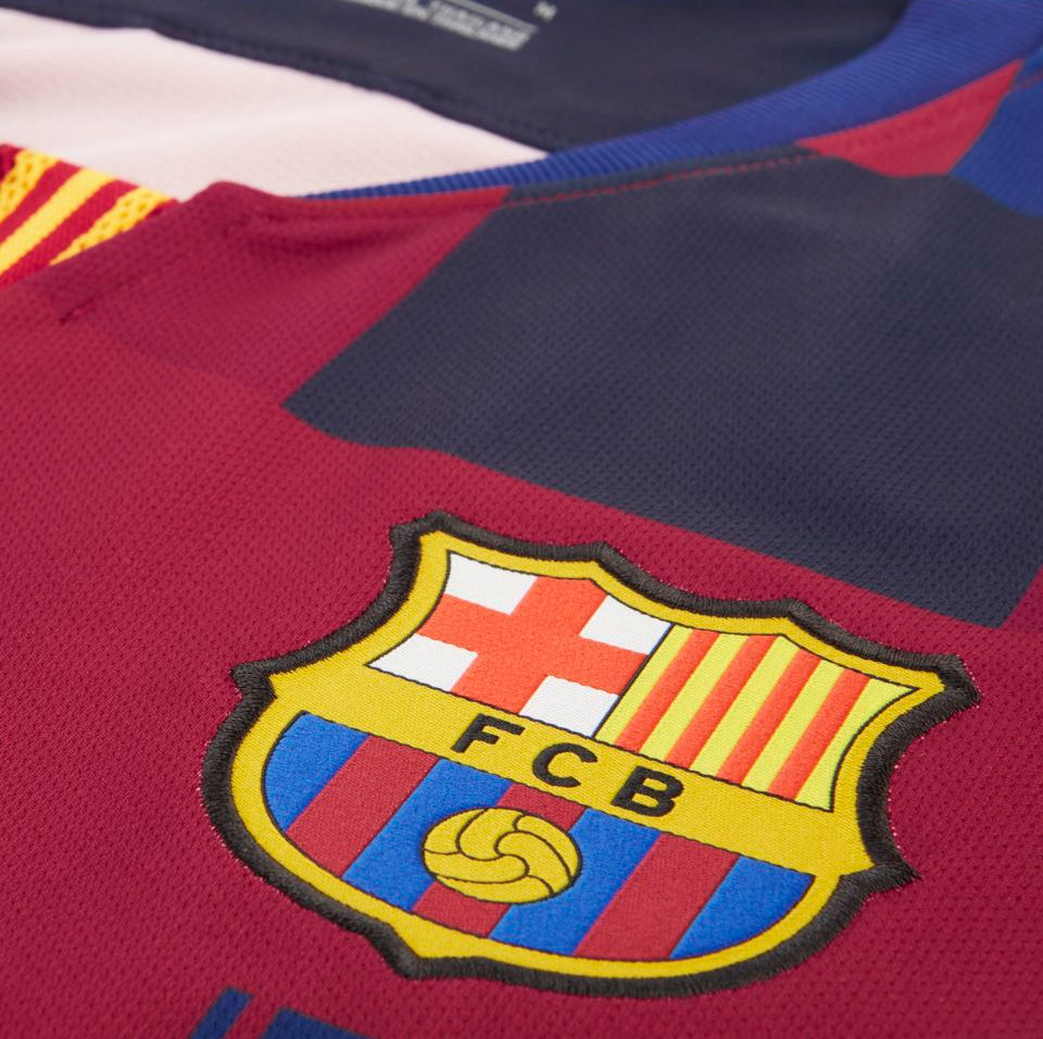 Primer plano del escudo oficial del FC Barcelona sobre el patrón textil en bloques del jersey conmemorativo mashup de local 1999 2019 de Ronaldinho  (Ref. 943025-456) en Futbol90MX