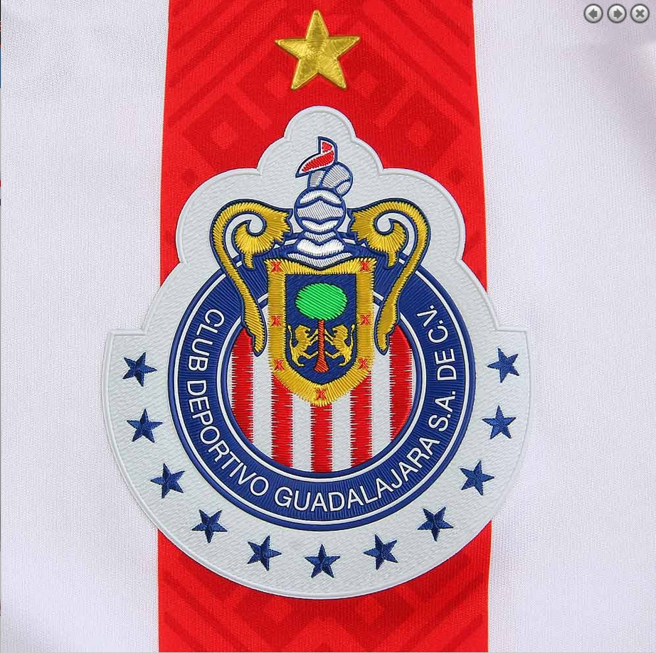 Detalle de cerca del pecho del jersey de casa de Chivas 2017/18, mostrando el escudo oficial con estrellas y el diseño texturizado sutil sobre las franjas rojas.