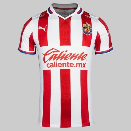Primer plano del pecho del jersey de Chivas 2020/21, destacando el escudo oficial bordado, el logotipo de Puma Cat y el patrocinador principal 'Caliente.mx', stock Futbol90MX