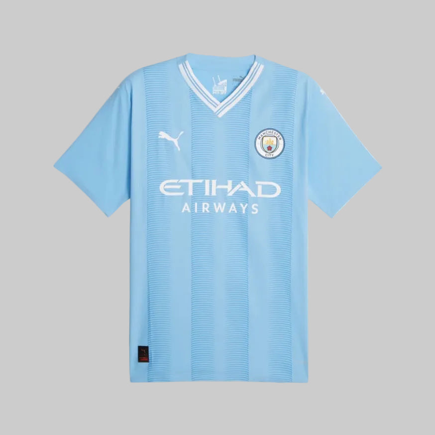 Vista completa del jersey de casa del Manchester City 23/24, destacando el corte atlético Slim Fit y el cuello en V con detalles blancos.