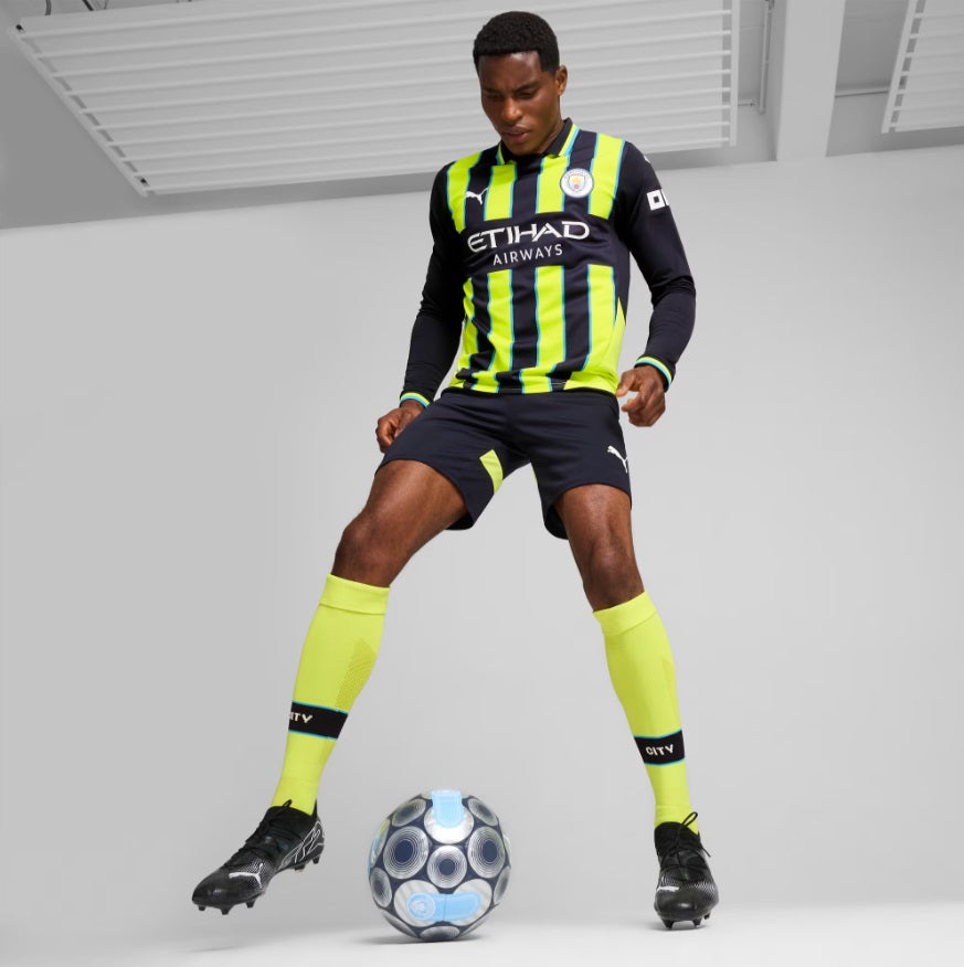 Modelo de cuerpo entero vistiendo el uniforme de visitante de manga larga del Manchester City 2024/25 (Ref. 775087 02) controlando un balón